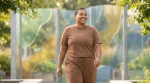 Une jeune femme souriante marchant dans un parc verdoyant, incarnant la santé et l'énergie positive.